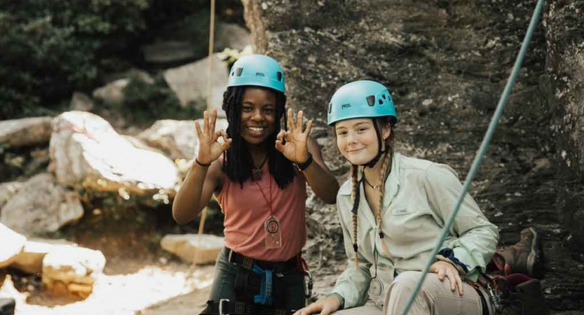 two students wearing rock climbing gear smile at the camera on an outward bound expedition in the blue ridge mountains